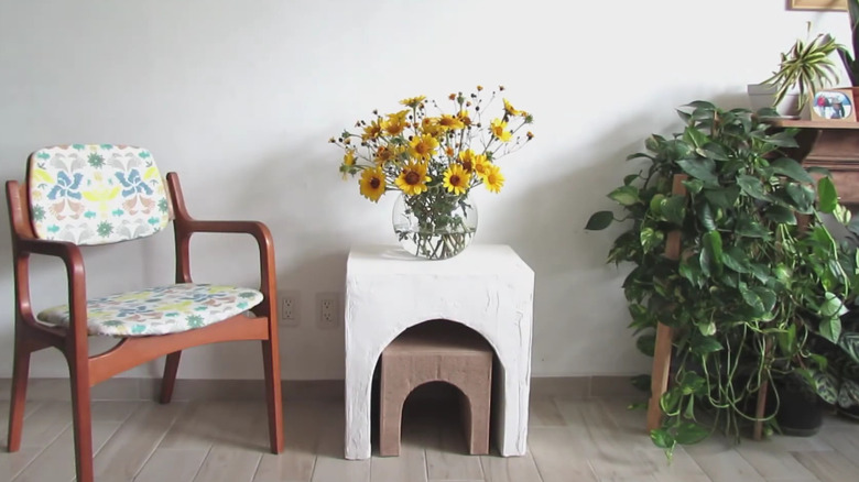 White arched cardboard end table with nesting table underneath and vase of yellow flowers