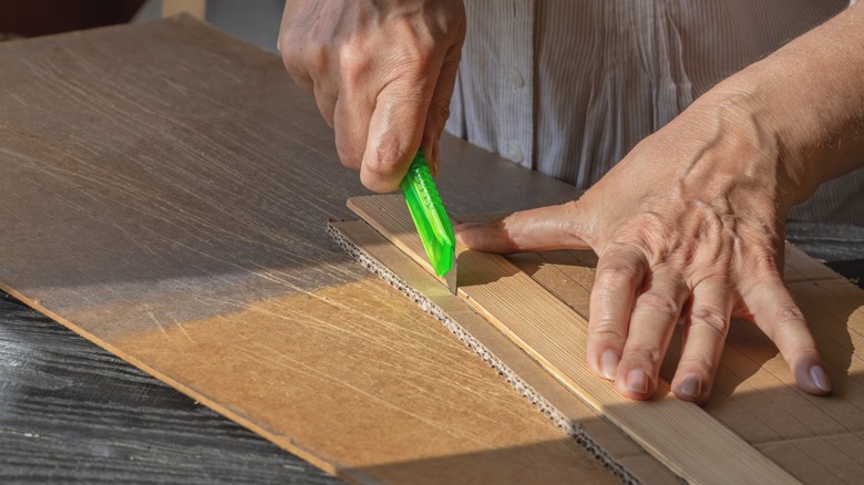 Person cutting cardboard with green utility knife over laminate cutting surface