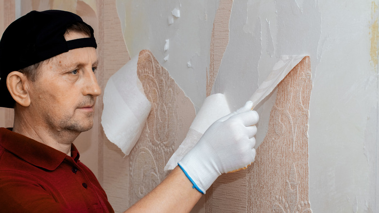 male struggling to remove wallpaper with uneven tears