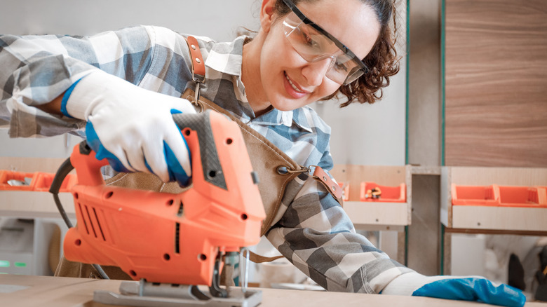 Smiling brown-haired woman cutting a board with a jigsaw.