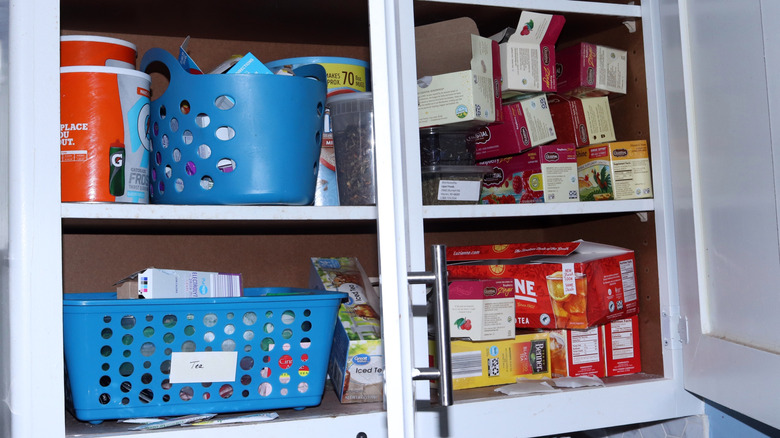 A cluttered kitchen cabinet filled with tea and other lightweight items