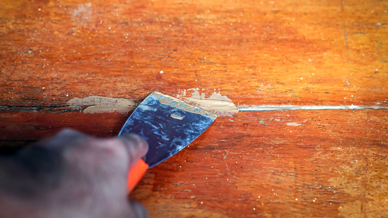 Person applying wood filler with a spatula on flooring