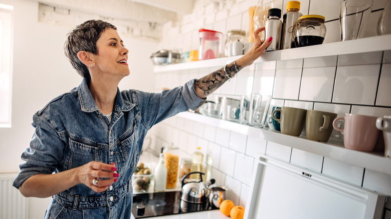 woman wearing denim reaching for an item on a shelf in her open shelving kitchen