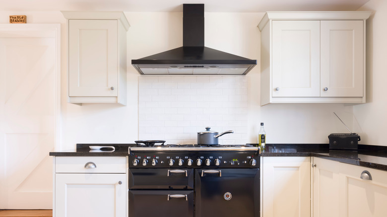 modular kitchen design with white cabinets, a black extractor hood over a black cooker oven, and a black stone countertop