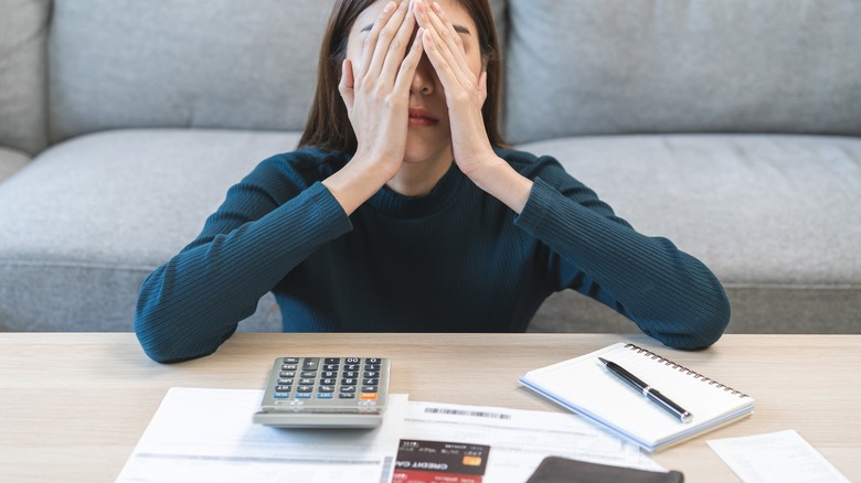 Woman with her hands on her head and a calculator and papers in front of her