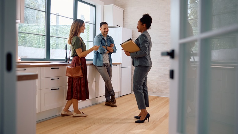 A couple talking to a real estate agent in an empty home's kitchen