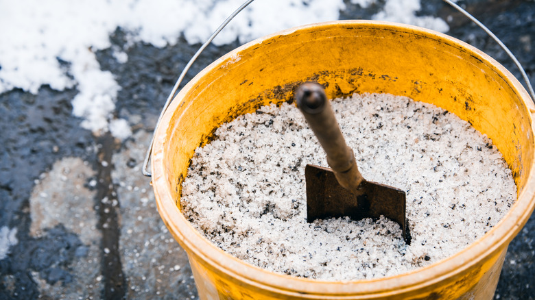 A yellow bucket full of deicing salt with a hand shovel in it