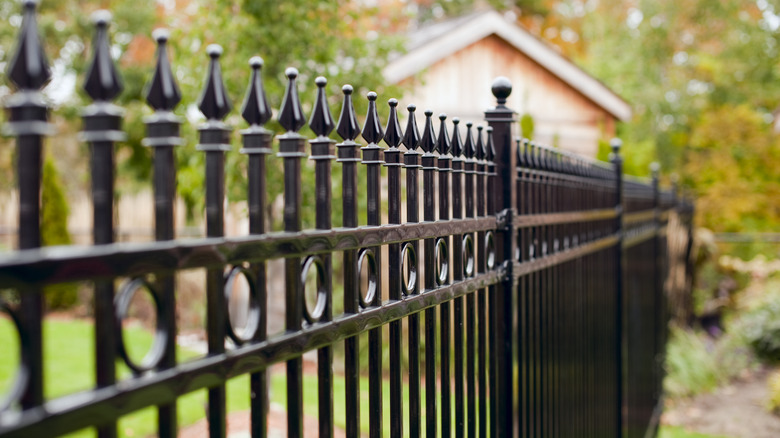 black metal fence with a house and greenery in the background