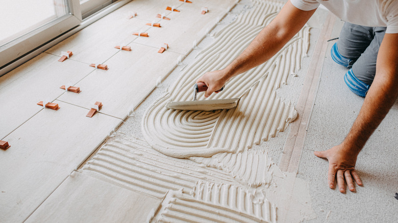 A worker tiles a floor in a home kitchen with ceramic tiling.