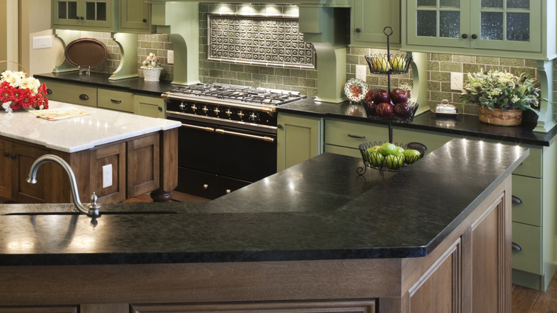 Double-level kitchen island with soapstone countertops and more soapstone counters in background