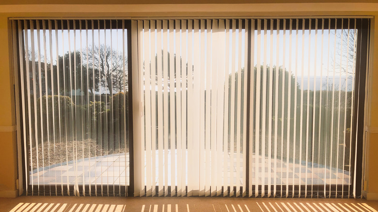 A sliding glass door with vertical blinds facing a yard