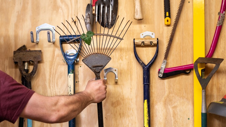 person grabbing rake from wall