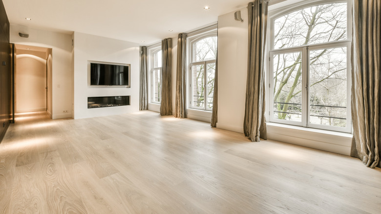 Bland light wood flooring in spacious living room with curtains.