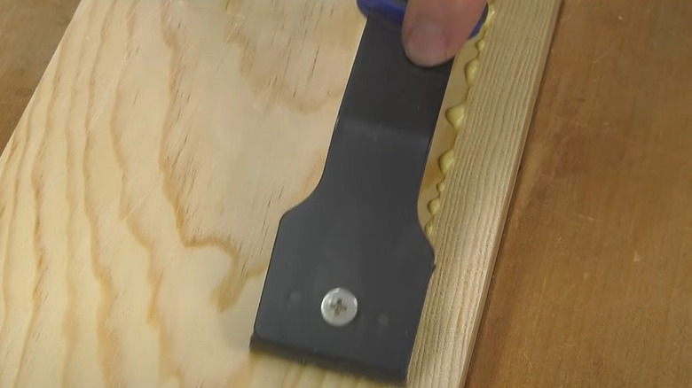 Person using scraper to remove glue from wood