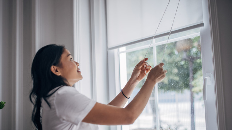 Woman extending roller blinds in home