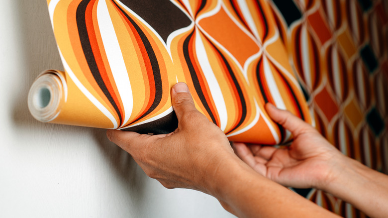 Person applying patterned wallpaper to white wall