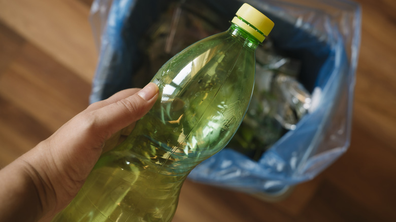 Hand holding soda bottle over trash can