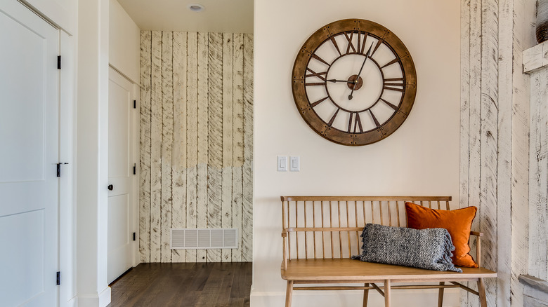 A foyer with wooden accent walls and oversized clock above bench