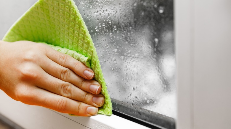 A person uses a rag to wipe condensation off a window.