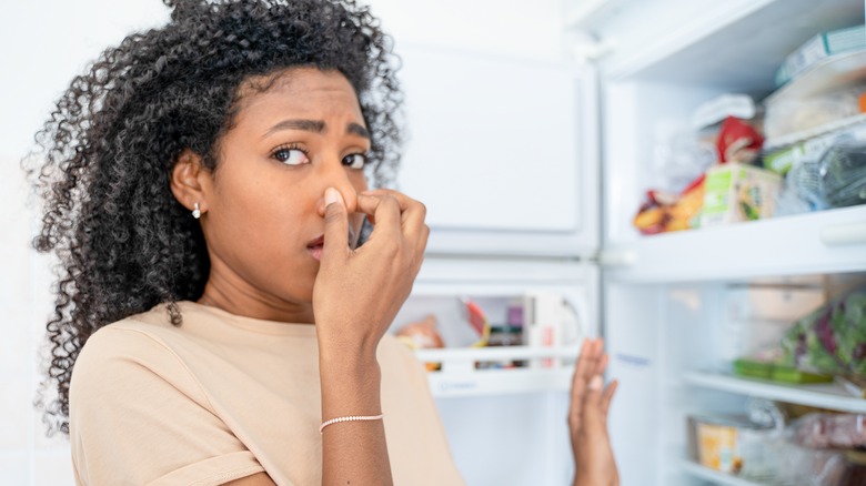 woman holding nose in front of fridge