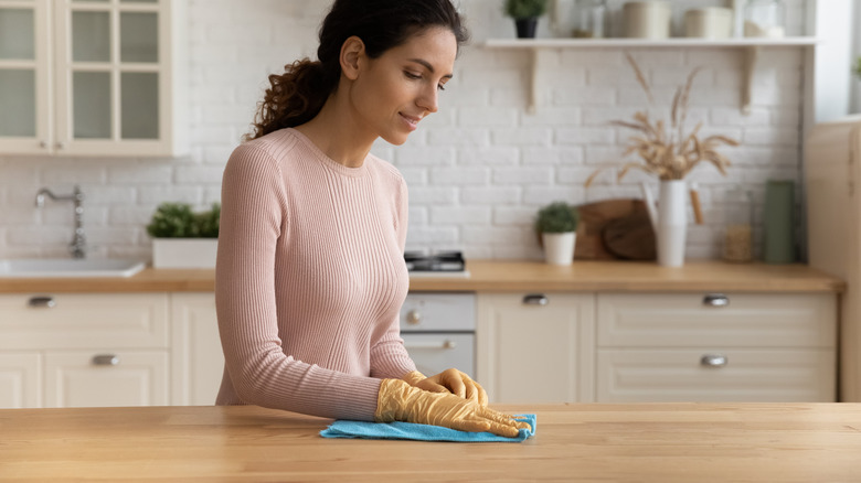 The woman uses a dish cloth to clean the wood countertop in her kitchen.