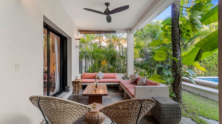 A modern patio with a black ceiling fan and sleek seating surrounded by greenery