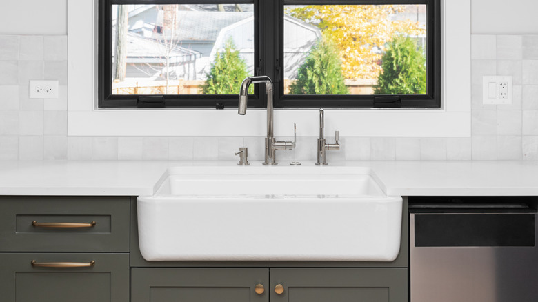 A white farmhouse sink nestled on top of dark cabinets and a white countertop