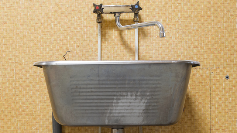 A wash tub style sink stands alone against an orange wall