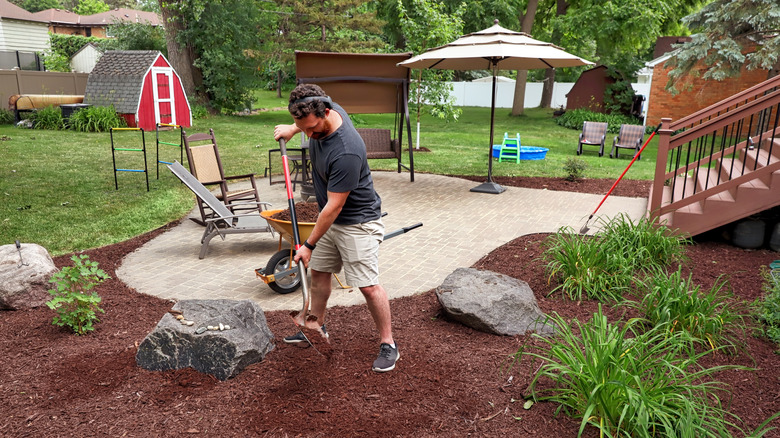 A man digs a shovel into the ground as he prepares his backyard garden for landscaping.