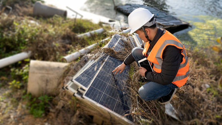 Man inspecting weather-damaged solar panels on the ground