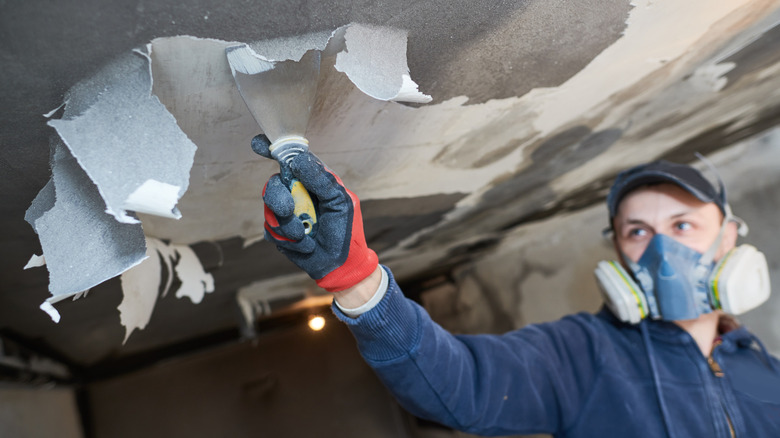 A fire restoration contractor removes wet, soot covered ceiling paint