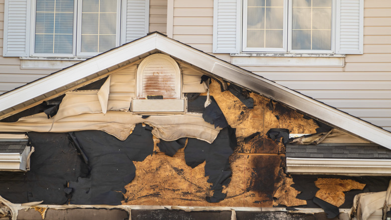 Extensive fire damage, including melted siding, is seen on a beige house