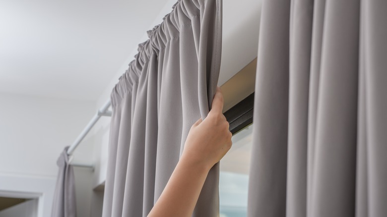 hand pulling hanging gray curtains