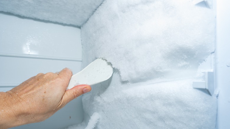 person scraping ice off freezer wall