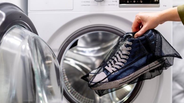 A person putting mesh bag containing blue sneakers into dryer.