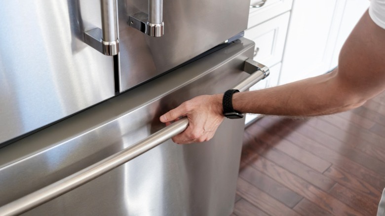 A man's arm opening bottom freezer in stainless steel French door refrigerator.