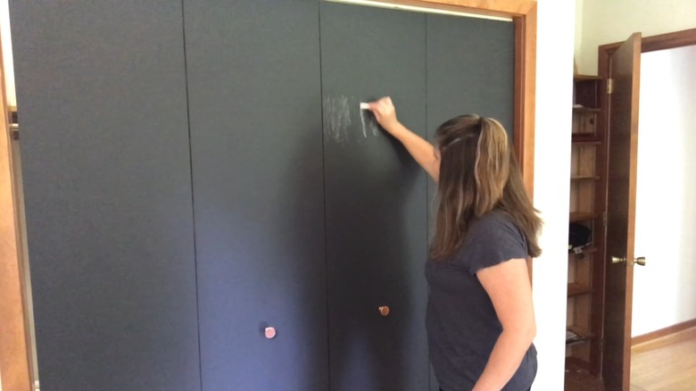 Woman draws on her chalkboard closet doors with a piece of white chalk