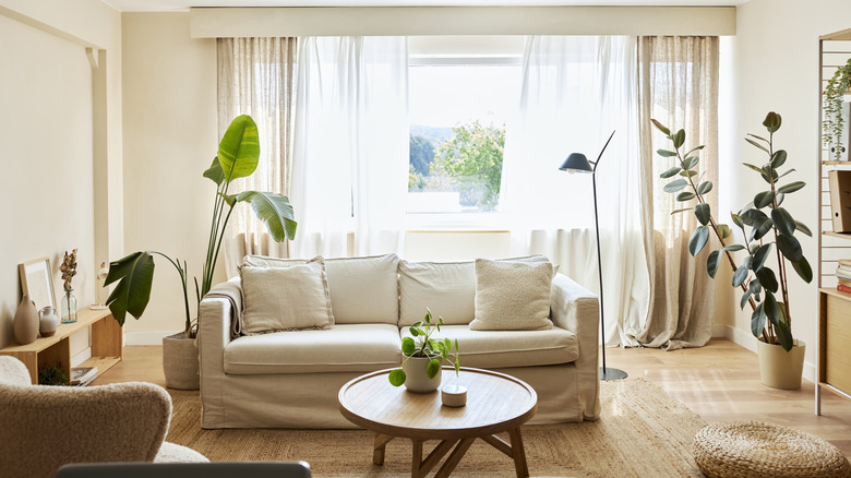 A well-lit living room has a beige couch, potted plants, and wood furniture.