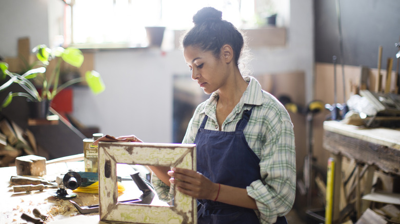 A woman sands an old wooden frame