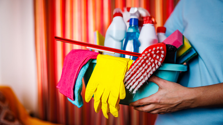 Someone holding a small bin of cleaning supplies