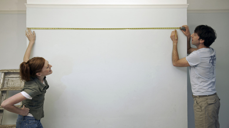 A couple measuring an empty wall space.