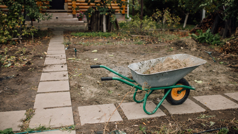 Wheelbarrow with dirt on stepping stones in barren yard