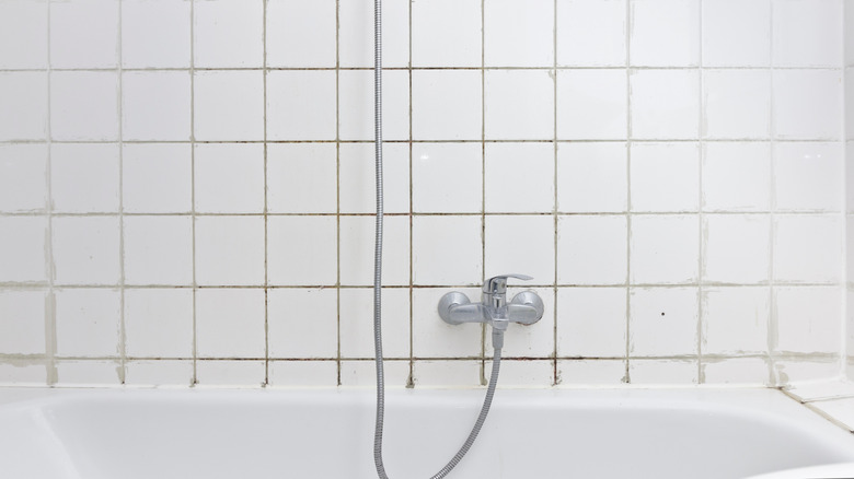 Dirty bathroom tile and grout above bathtub.