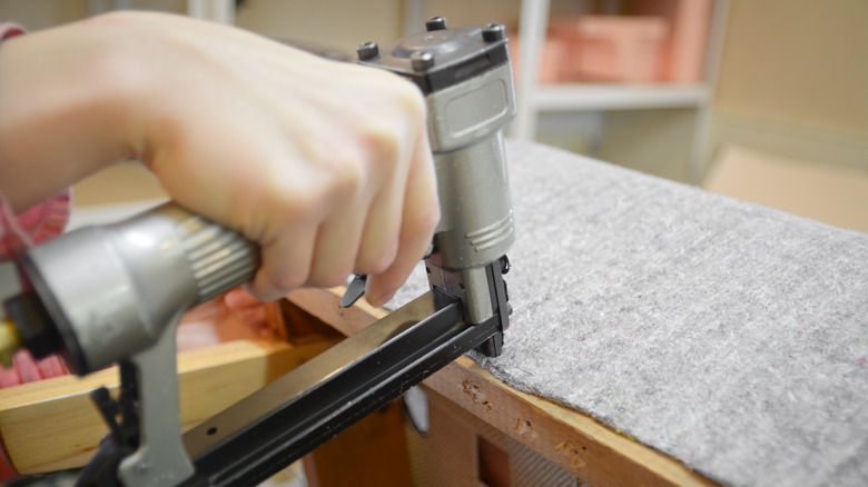 person stapling fabric onto furniture 