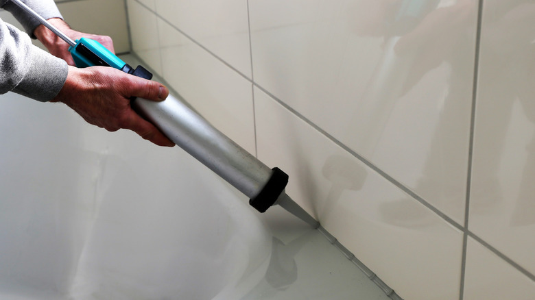 A pair of hands applying grey caulk on a bath tub.