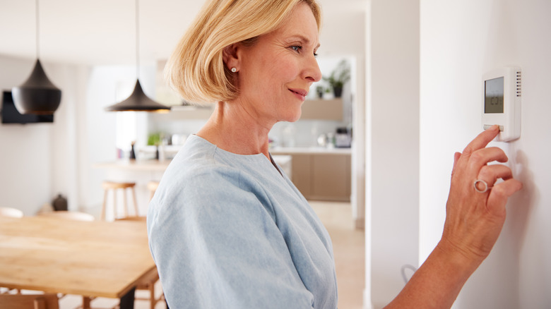 woman adjusting thermostat in home