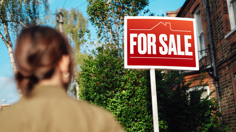 Back view of a woman looking at home with a "For Sale" sign