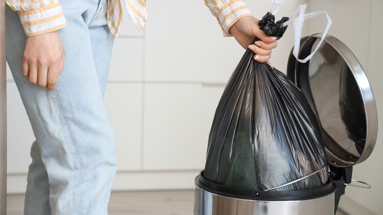 Woman taking trash bag out of trash can