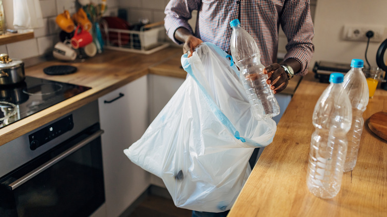 Man throwing empty plastic bottles into a white trash bag