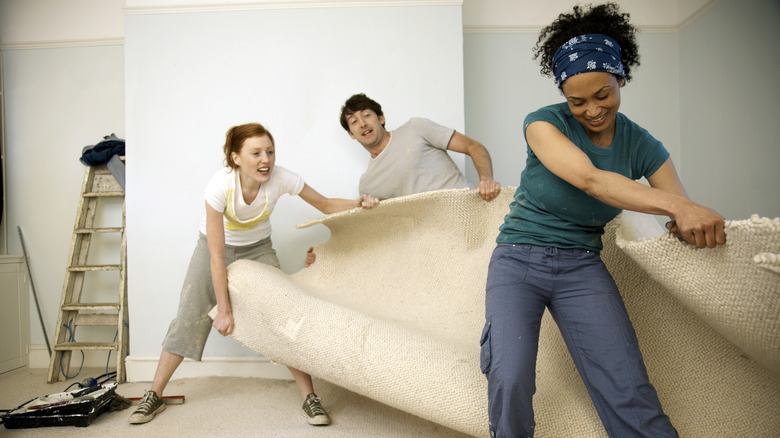 three people moving white carpeting